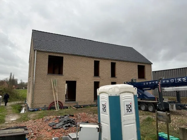 Twee halfopen nieuwbouwwoningen in Kampenhout met een afgewerkt grijs pannendak en gevels in aanbouw.