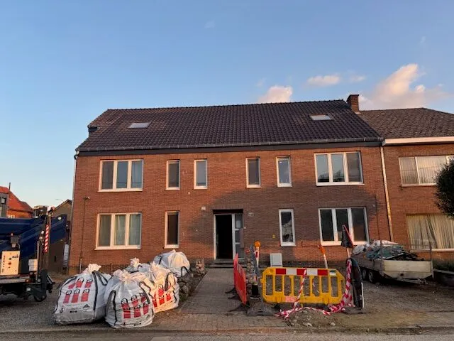 Bakstenen appartementsgebouw met een rood pannendak en dakramen, gezien vanaf de straat.