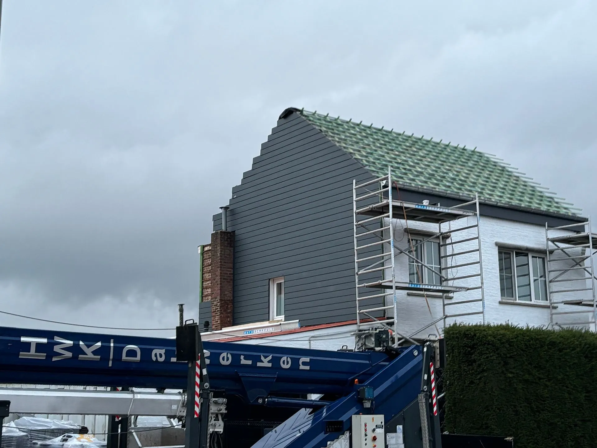 Woning tijdens renovatie met grijze gevelbekleding en groene onderdakfolie onder de panlatten.