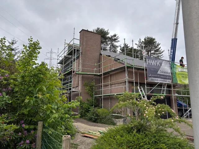 Woning omringd door steigers tijdens dak- en gevelrenovatie, met een hoge gemetselde schoorsteen.