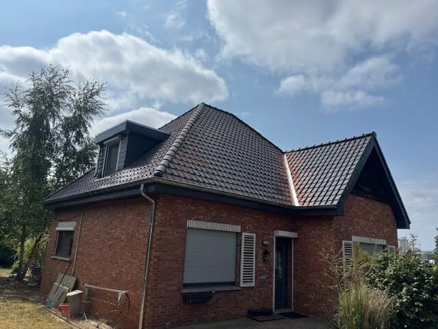 Zijaanzicht van een woning in Meldert met grijze dakpannen, een dakkapel en afgewerkte dakgoten.