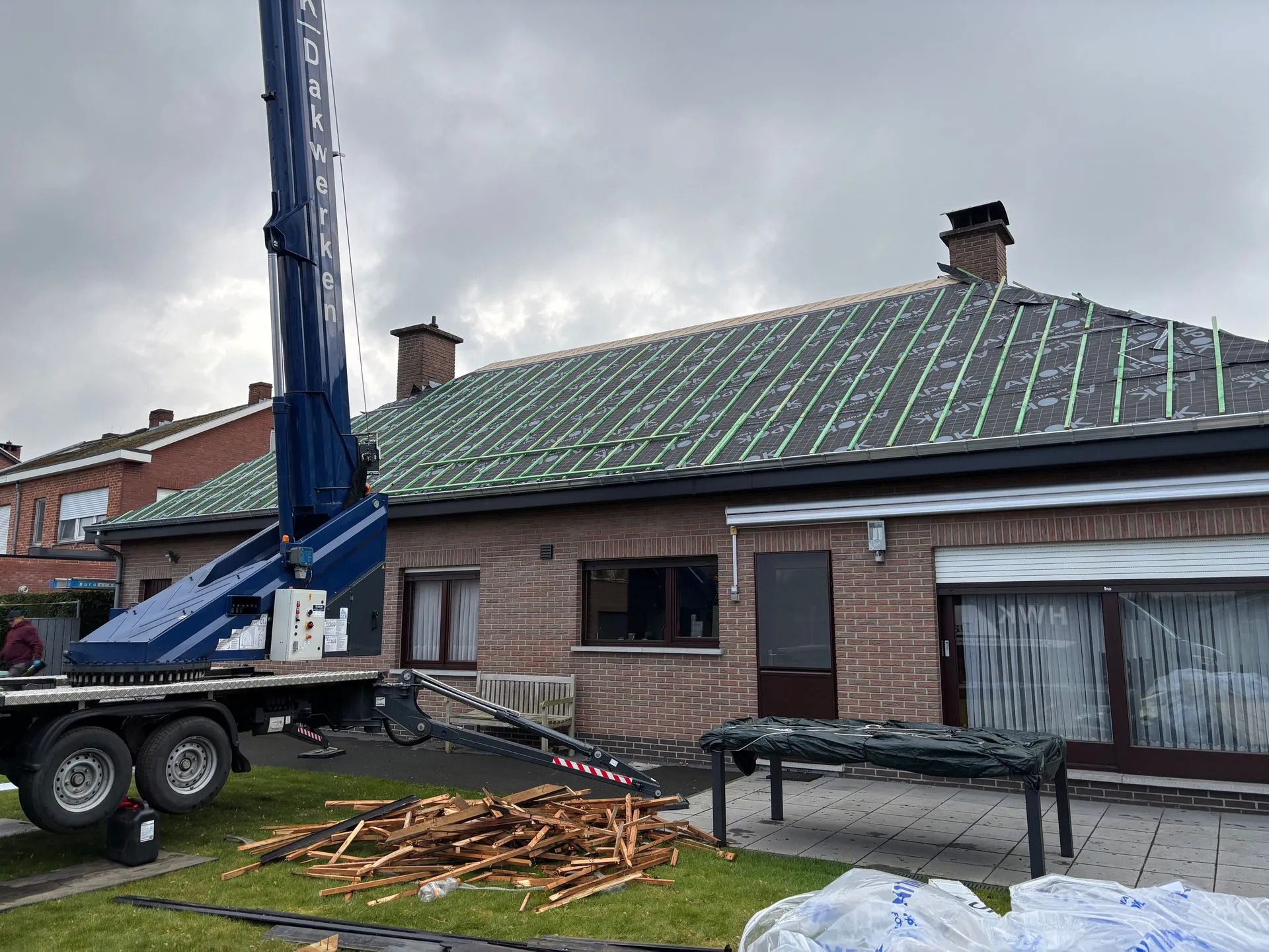 Achterzijde van een woning tijdens dakrenovatie, met onderdakfolie, panlatten en een hijskraan.