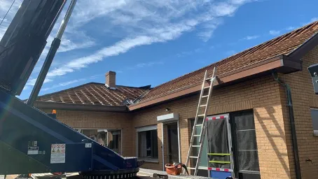 Deels ontmanteld dak van een woning in Lummen, met zichtbare houten dakconstructie, ladders en een hijskraan.