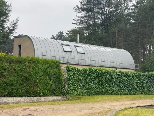 Zijaanzicht van een woning in Hechtel-Eksel met een gebogen zinken dak met staande naden en twee dakramen.