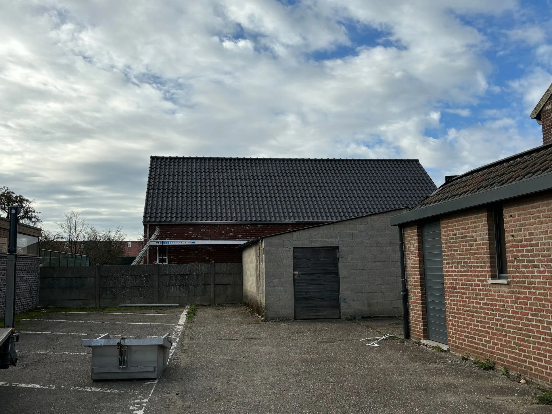 Binnenplaats bij een garage en paardenstal in Borgloon, met zwarte pannendaken boven de bijgebouwen.