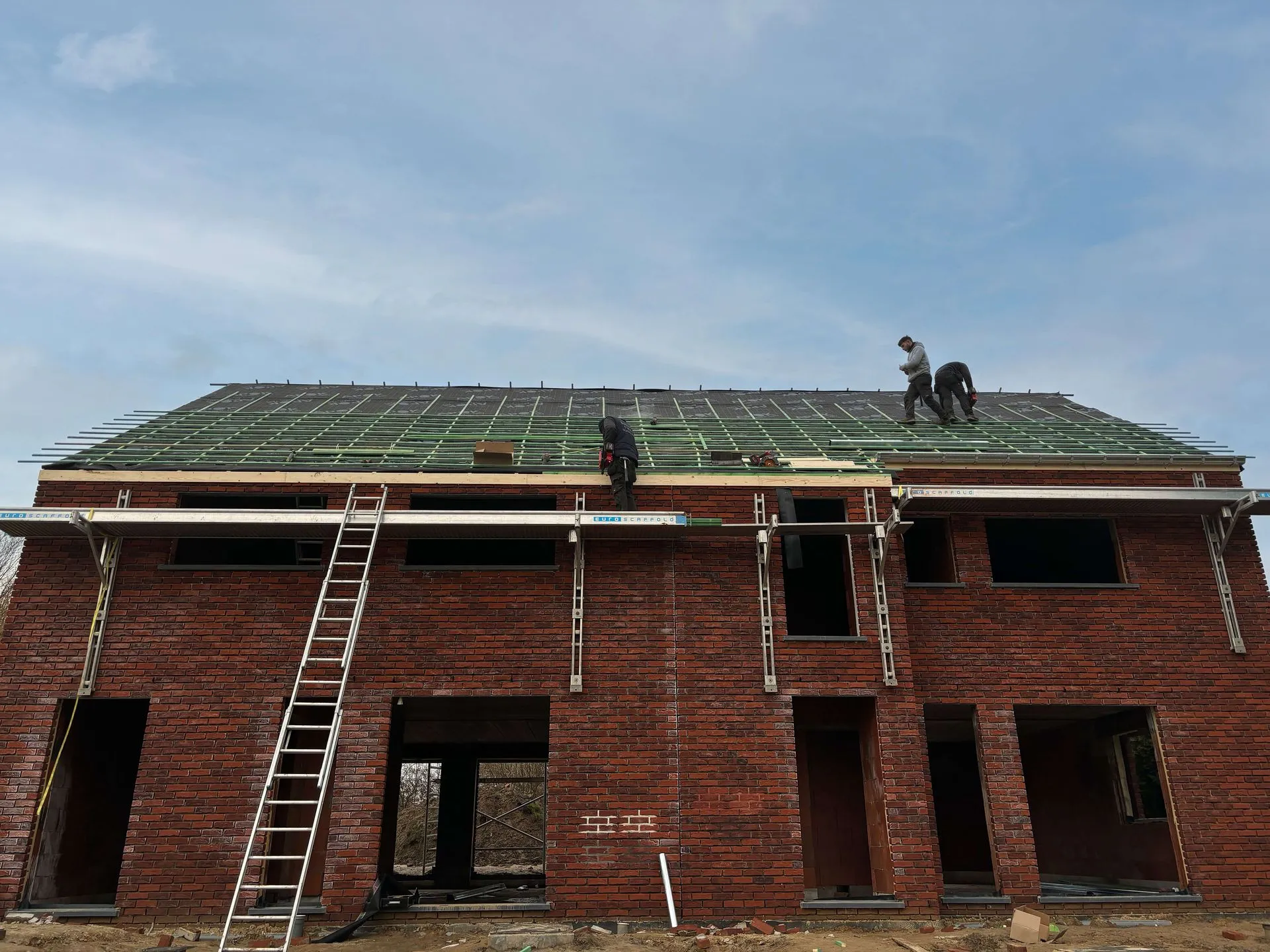 dakwerkers die bezig zijn met een dak te plaatsen op een nieuwbouwwoning