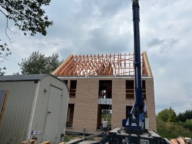 Houten dakspanten op een nieuwbouwwoning, met een hijskraan naast de bakstenen ruwbouw.