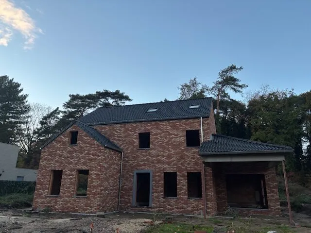 Bakstenen nieuwbouwwoning met afgewerkte donkere pannendaken, dakramen en een aangebouwde carport.