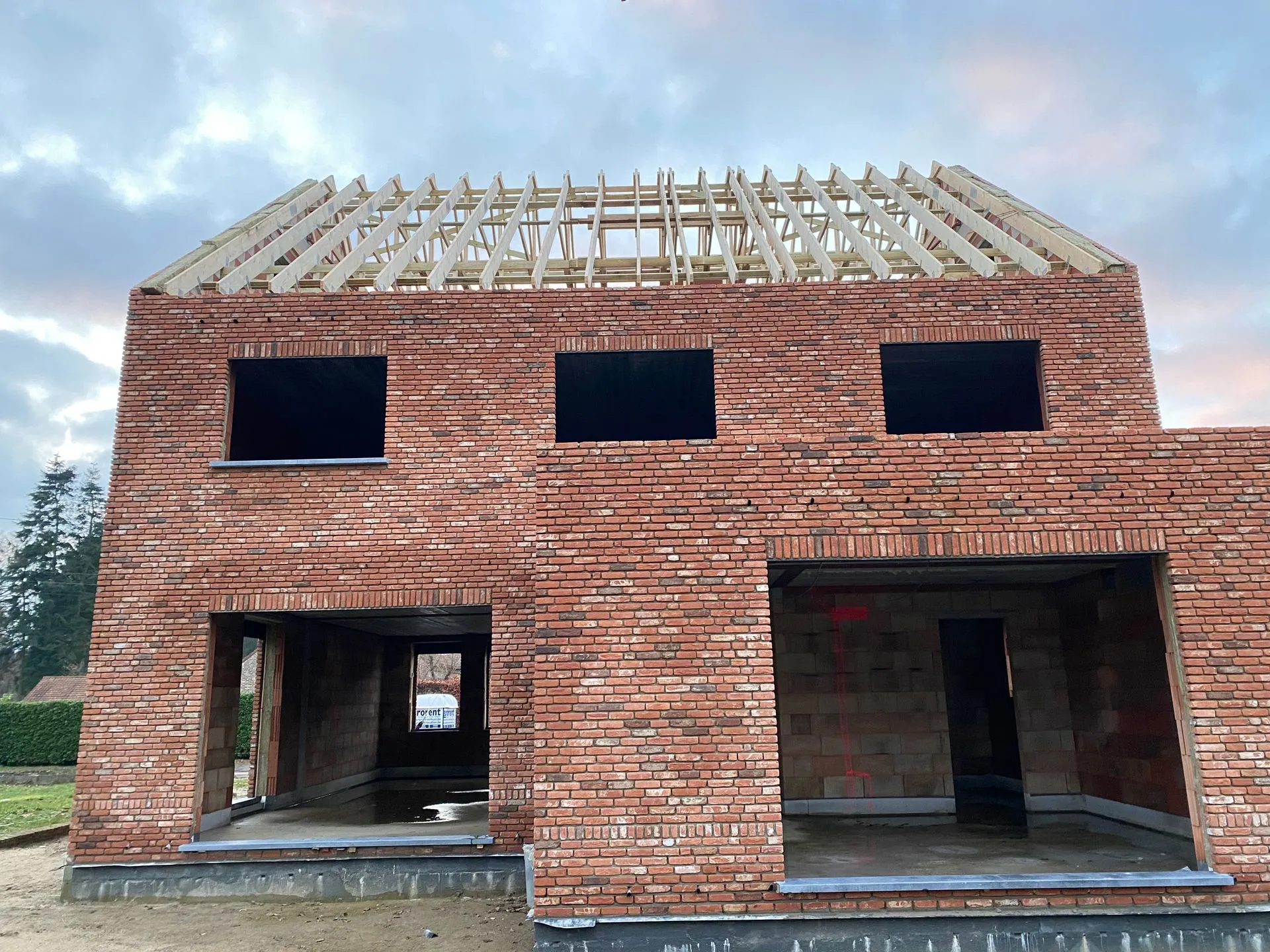 Voorgevel van een woning in aanbouw in Averbode, met houten dakspanten boven de open raam- en garageopeningen.
